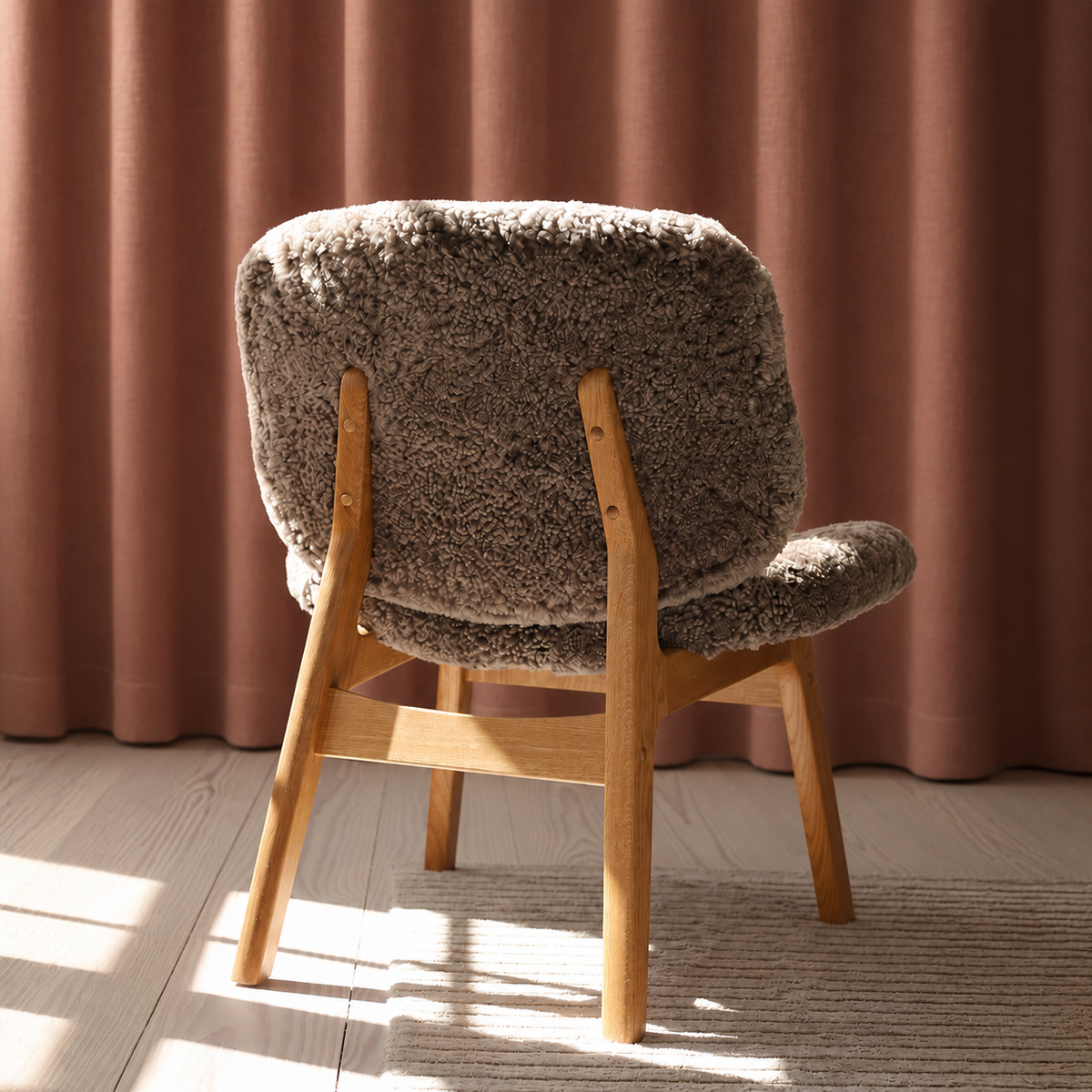 Loungestolen Pandora Lounge med blødt fåreskind, trædetaljer og rustrøde nuancer i et roligt skandinavisk design.